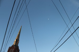 Juxtaposition of cables, wires, church steeple, and moon in the morning sky